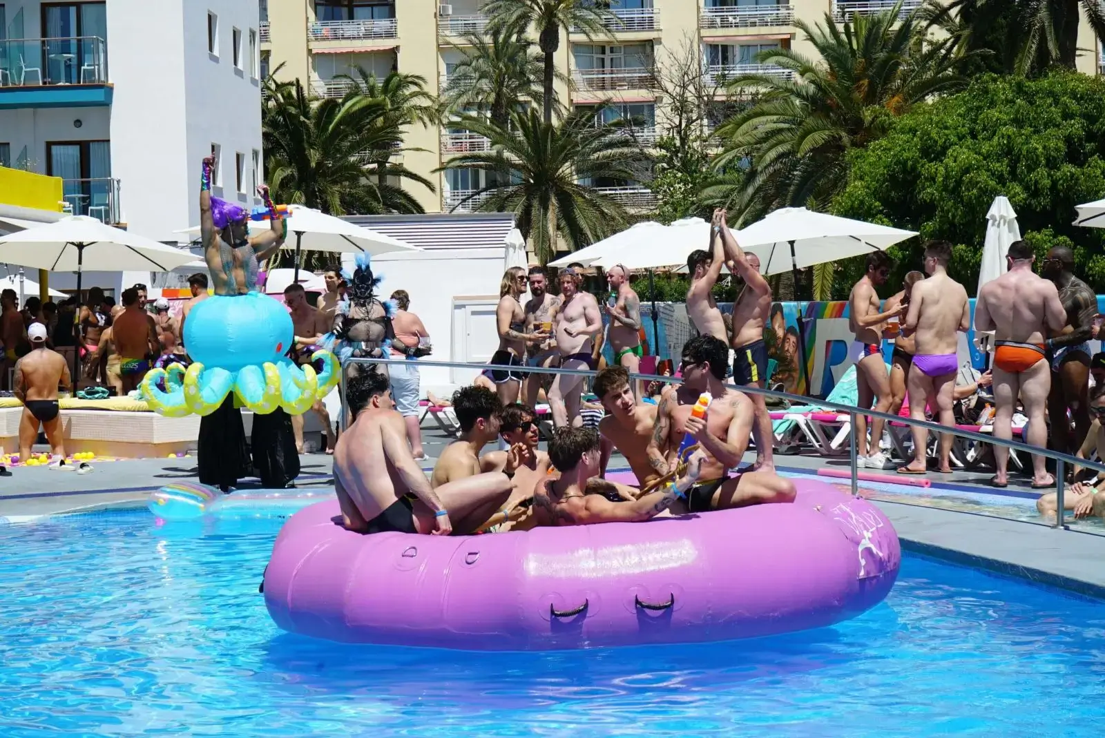 Group of friends enjoying a sunny day on a large pink inflatable in a pool.